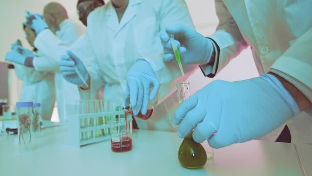 Hands of scientists performing experiments in a laboratory setting, handling colorful chemical solutions in glass containers