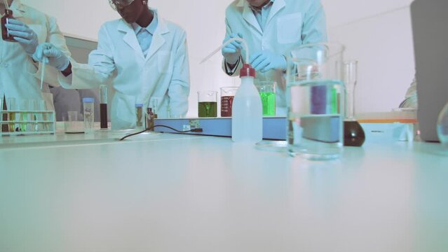 Slow motion zoom-in on scientists in a laboratory with a focus on the detailed work being performed with chemical solutions in beakers