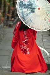 Vertical shot of a geisha walking in the street with a red dress and umbrella - shot from back