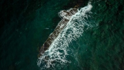 Aerial shot of foamy waves crashing on a stone barrier