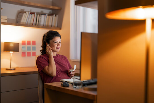 A happy mid adult woman putting on her earphones to follow a web conference on her computer