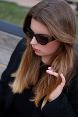 young blonde woman in a black classic jacket and black stylish sunglasses on the street. close-up portrait of a blonde woman. casual style
