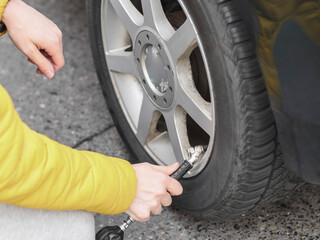 The hands of a man pump air into the wheel of the car with a compressor.