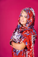 A woman wearing a red, blue and white scarf stands in front of a pink background, copy space.
