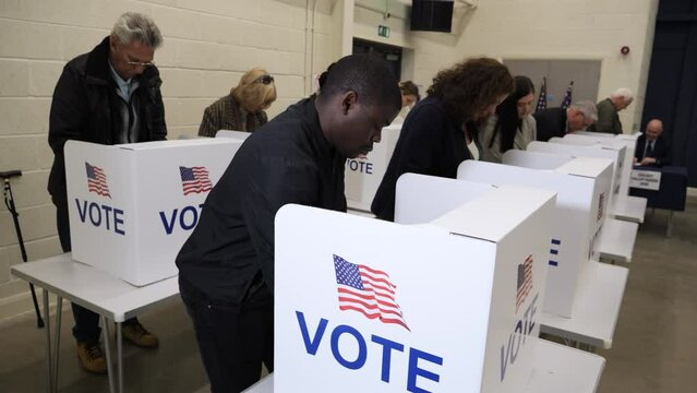 4K: Black Male Voting at Polling Place for the USA Presidential Election. 25-29 years. People Vote near him. Gimbal around. Stock Video Clip Footage