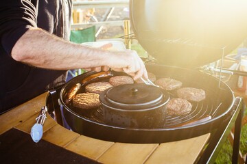 Closeup of a male's hands cooking burgers and hot dogs on a grill