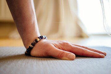 Closeup shot of a woman's hand on a yoga mat with a bead bracelet