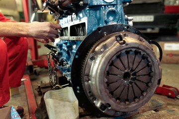 Fototapeta na wymiar Young mechanic in a red uniform mounting the car engine