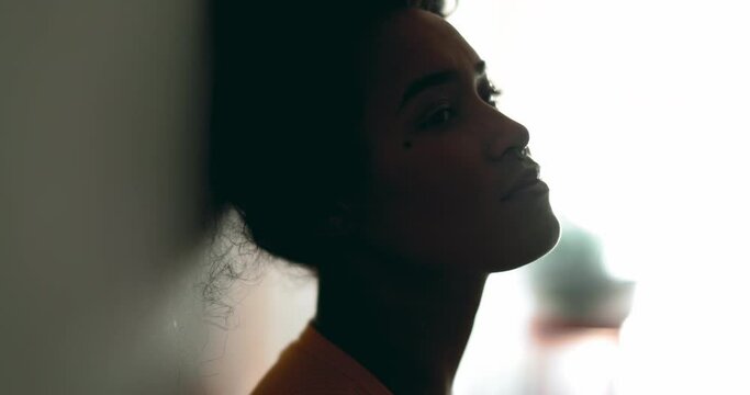 One depressed young black latina woman leaning on wall with melancolic expression gazing at distance feeling lost in thought, profile close-up face in silhouette
