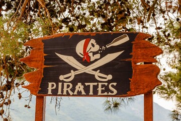 Closeup shot of a wooden board with a pirates sign, a scull drinking alcohol and swords