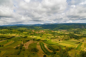 Fototapeta na wymiar Aerial shot of the green fields with a small village and mountains in the background