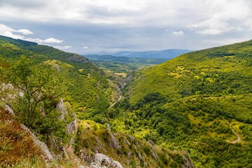 Aerial shot of a narrow road surrounded by the big green mountains under the cloudy sky