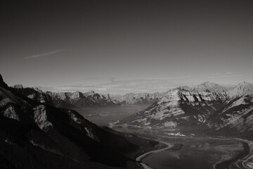 Grayscale shot of roads surrounded by rocky mountains covered in the snow