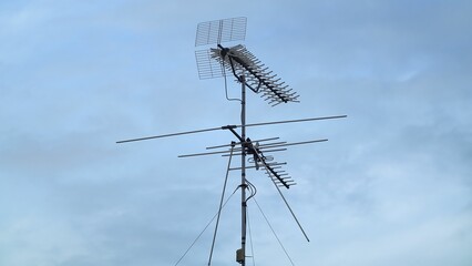Multiple antennas standing on top of the rooftop against the blue cloudy sky