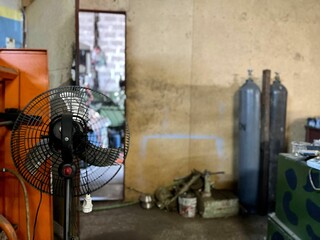 Fan with two oxygen cylinders in the blurred background and an opened door in a master workshop