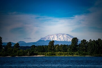 Scenic shot of a snowy peak in the background of a lake with a green coastline