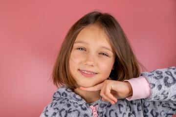 Portrait of a beautiful smiling brunette girl 8 years old on a pink background in pajamas close-up