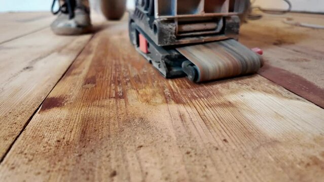 Dynamics of wooden floor restoration. The work of a sander to remove old floor paint. Renovation of the wooden surface. Modern renovation, Sanding a floor with a grinding machine close-up video.