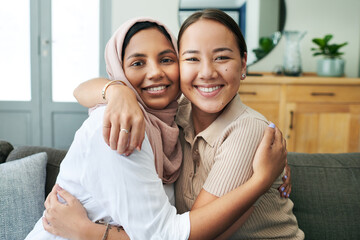Obraz premium Diversity, portrait and women hugging on sofa in living room of home together for bonding or visit. Love, relax and smile with happy young friends embracing in apartment for peace, support or trust
