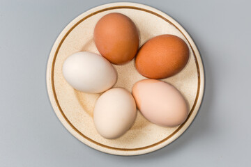Whole boiled chicken eggs different colors on saucer, top view