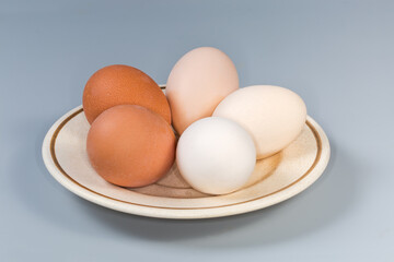 Whole boiled chicken eggs different colors on saucer, side view