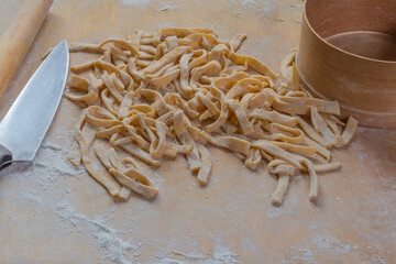 Raw freshly prepared homemade egg noodles on a wooden board - 781234595
