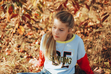 teenage girl with blue eyes and blond hair in an autumn garden. the girl near the trees with yellow...