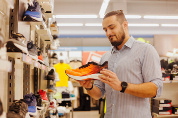Young man shopper choosing new sneakers at modern sports shop
