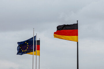 European Union and German flags fluttering against a cloudy sky.
