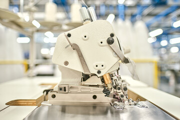 Hands on a sewing machine working in a textile factory industrial setting. Metal cotton sewing machine industry. Cotton sewing and fabrication textile industries. Metal hanger rails.