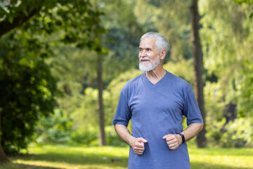 Smiling and satisfied senior gray-haired man in casual clothes running in the park and doing sports.