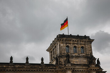 The flag of Germany flutters proudly near the German Parliament building against a cloudy sky.