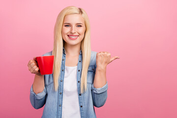 Photo of young girl point thumb empty space advise suggest promotion drink cup tea isolated over pink color background
