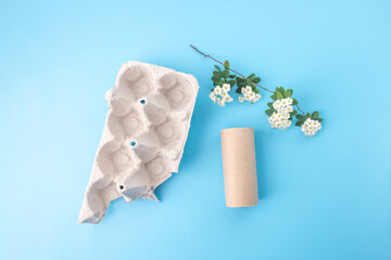 Egg carton, white blossoms, toilet paper roll, craft materials variety, blue background, top view