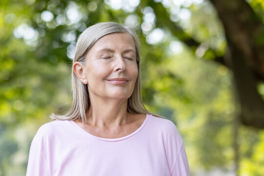 Close-up photo of an older woman standing in nature with her eyes closed and meditating and resting thoughtfully and relaxed.