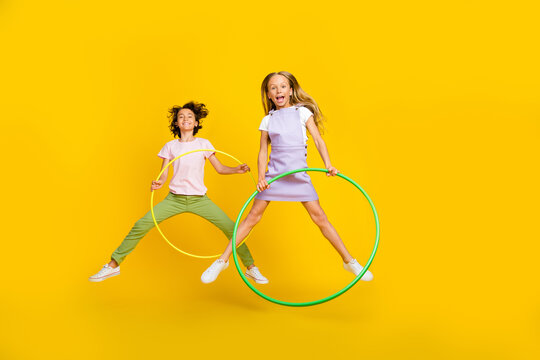Full length photo of cute funky friends wear casual outfits jumping high playing hoola hoops isolated yellow color background