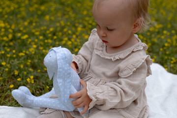 cute little girl in a beige dress plays with a soft hare in yellow flowers