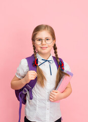 Positive school girl in eyeglasses with rucksack smiling over pink background. Happy schoolkid portrait.
