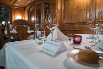 Elegant dining table set in luxury hotel, likely in Zermatt, Swiss ski resort. White tablecloth, glassware, folded napkin, silverware, and candle holder.