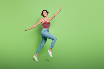 Fototapeta na wymiar Full length photo of carefree positive cute girl wear stylish outfit flying air going empty space isolated on green color background