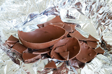 Un uovo di Pasqua di cioccolato al latte rotto in pezzi su fondo argentato. Pasqua e periodo festivo. - 781248703