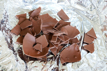 Un uovo di Pasqua di cioccolato al latte rotto in pezzi su fondo argentato. Pasqua e periodo festivo. - 781248710
