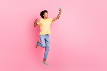 Full body portrait of handsome excited guy jumping hold smart phone make selfie isolated on pink...