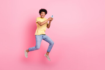 Fototapeta na wymiar Full size photo of active sporty person hold smart phone jumping empty space isolated on pink color background