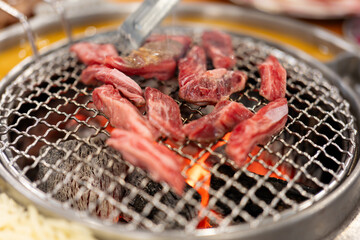 In the barbecue restaurant, the waiter lays a barbecue net on the red environmentally friendly barbecue charcoal, and uses food tongs to place the steak and bones, teaching delicious and juicy 