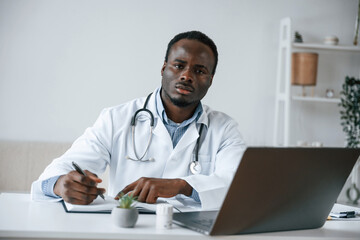 Writing information into the document. Black man as doctor in the clinic office