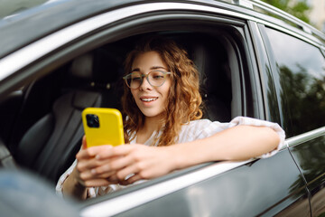 Portrait of young woman is driving a car with phone.  Leisure, travel, technology, navigation.