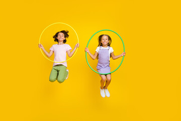 Full length photo of cheerful cute friends wear casual outfits jumping high rising hoola hoops...