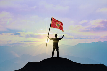 Montenegro flag being waved by a man celebrating success at the top of a mountain against sunset or sunrise. Montenegro flag for Independence Day.
