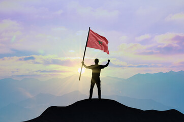 Morocco flag being waved by a man celebrating success at the top of a mountain against sunset or sunrise. Morocco flag for Independence Day.